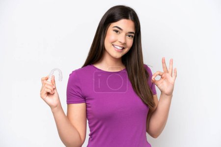 Photo for Young Brazilian woman holding invisible braces isolated on white background showing ok sign with fingers - Royalty Free Image