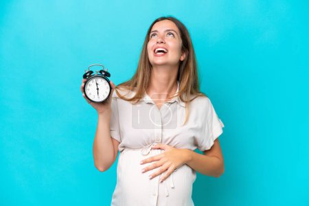 Photo for Young caucasian woman isolated on blue background pregnant and holding clock with stressed expression - Royalty Free Image
