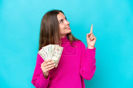 Téléchargez les photos : Jeune femme caucasienne prenant beaucoup d'argent isolé sur fond bleu pointant vers le haut d'une grande idée - en image libre de droit