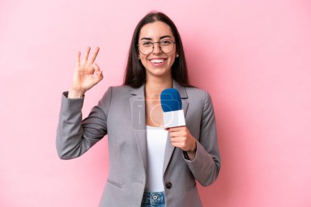 Téléchargez les photos : Jeune présentateur de télévision caucasienne femme isolée sur fond rose souriant et montrant signe de victoire - en image libre de droit