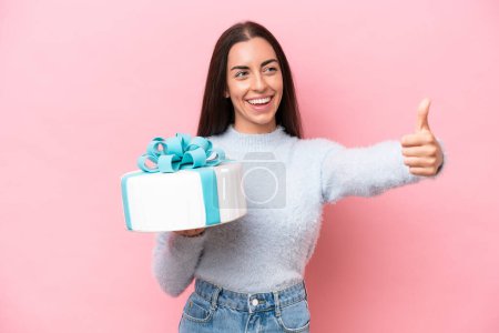 Photo for Young caucasian woman holding birthday cake isolated on pink background giving a thumbs up gesture - Royalty Free Image