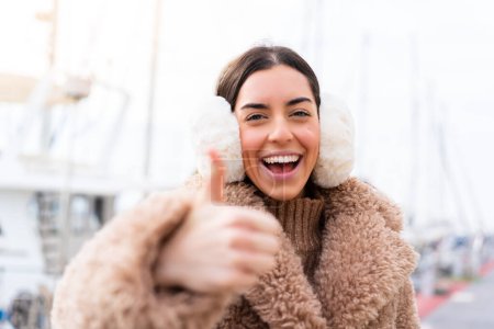 Téléchargez les photos : Jeune femme portant des manchons d'hiver à l'extérieur avec les pouces levés parce que quelque chose de bon est arrivé - en image libre de droit
