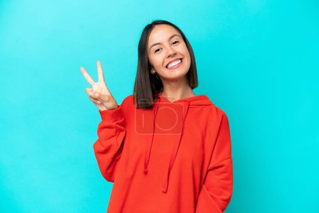 Téléchargez les photos : Jeune femme caucasienne isolée sur fond bleu souriant et montrant signe de victoire - en image libre de droit