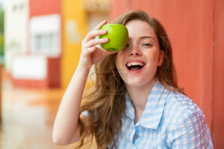 Téléchargez les photos : Jeune rousse femme à l'extérieur tenant une pomme avec une expression surprise - en image libre de droit