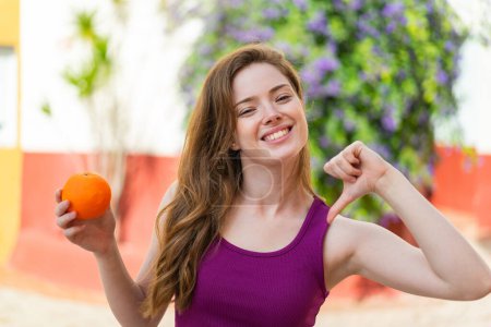 Téléchargez les photos : Jeune rousse femme tenant une orange à l'extérieur fier et satisfait de soi - en image libre de droit