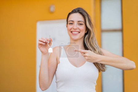 Foto de Joven bonita mujer sosteniendo las llaves del hogar al aire libre con expresión facial sorpresa - Imagen libre de derechos