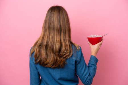 Photo for Young caucasian woman holding a bowl of cereals isolated on pink background in back position - Royalty Free Image