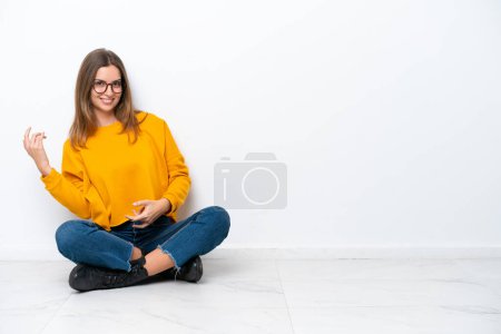 Téléchargez les photos : Jeune femme caucasienne assise sur le sol isolé sur fond blanc faisant geste de guitare - en image libre de droit