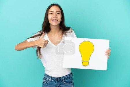 Photo for Young French woman isolated on blue background holding a placard with bulb icon with thumb up - Royalty Free Image