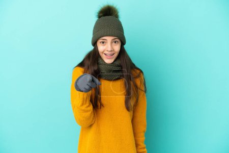 Photo for Young French girl isolated on blue background with winter hat surprised and pointing front - Royalty Free Image