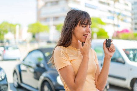 Téléchargez les photos : Jeune femme tenant des clés de voiture à l'extérieur avec surprise et expression faciale choquée - en image libre de droit