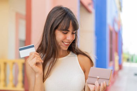 Photo for Young woman at outdoors holding wallet and credit card with happy expression - Royalty Free Image
