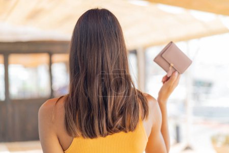 Photo for Young woman holding a wallet at outdoors in back position - Royalty Free Image