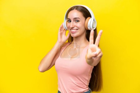 Téléchargez les photos : Jeune femme caucasienne isolée sur fond jaune écouter de la musique et chanter - en image libre de droit