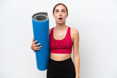 Photo for Young sport caucasian woman going to yoga classes while holding a mat isolated on white background looking up and with surprised expression - Royalty Free Image
