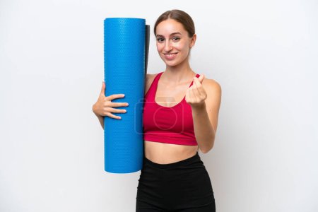 Photo for Young sport caucasian woman going to yoga classes while holding a mat isolated on white background making money gesture - Royalty Free Image