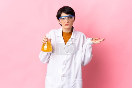 Téléchargez les photos : Jeune femme scientifique isolée sur fond rose ayant des doutes tout en levant la main - en image libre de droit