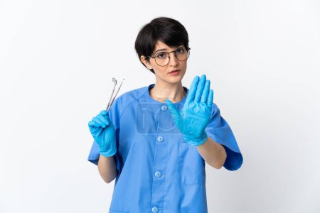 Foto de Mujer dentista sosteniendo herramientas aisladas sobre fondo blanco haciendo gesto de parada - Imagen libre de derechos