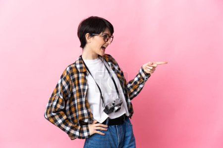 Photo for Young photographer woman isolated on pink background pointing finger to the side and presenting a product - Royalty Free Image