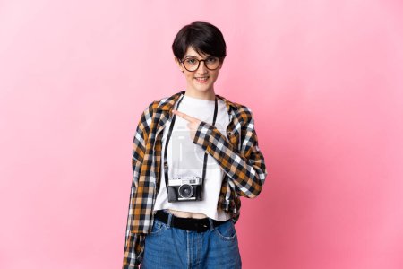 Photo for Young photographer woman isolated on pink background pointing to the side to present a product - Royalty Free Image