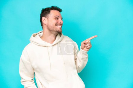Téléchargez les photos : Jeune homme beau caucasien isolé sur fond bleu pointant du doigt sur le côté et présentant un produit - en image libre de droit