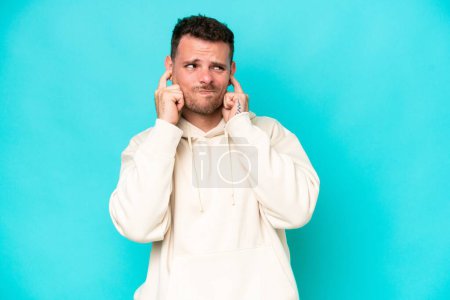 Photo for Young caucasian handsome man isolated on blue background frustrated and covering ears - Royalty Free Image