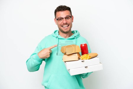 Foto de Joven hombre caucásico sosteniendo comida rápida aislada sobre fondo blanco con expresión facial sorpresa - Imagen libre de derechos