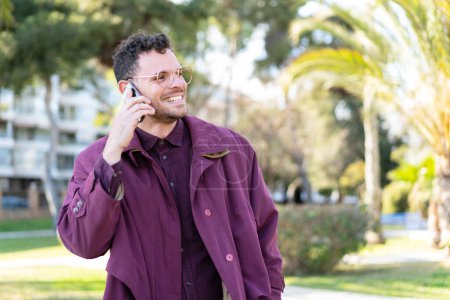 Téléchargez les photos : Jeune homme caucasien à l'extérieur gardant une conversation avec le téléphone portable avec quelqu'un - en image libre de droit