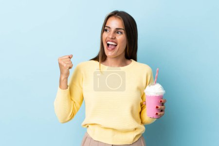 Téléchargez les photos : Jeune femme uruguayenne avec milkshake fraise isolé sur fond bleu célébrant une victoire - en image libre de droit