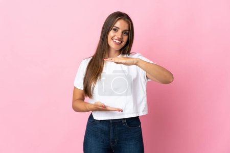 Téléchargez les photos : Jeune femme uruguayenne isolée sur fond rose tenant un copyspace imaginaire sur la paume pour insérer une annonce - en image libre de droit