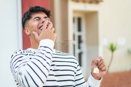 Téléchargez les photos : Jeune homme hispanique à l'extérieur tenant les clés de la maison avec expression heureuse - en image libre de droit