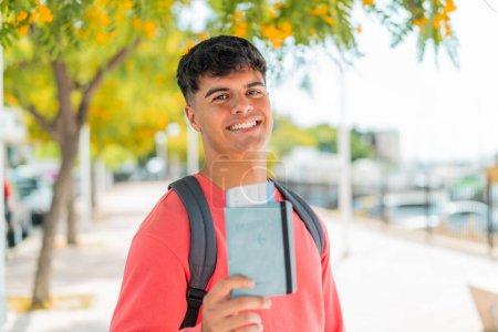 Photo for Young hispanic man holding a passport at outdoors with happy expression - Royalty Free Image