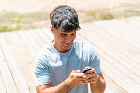 Téléchargez les photos : Jeune homme hispanique à l'extérieur envoyant un message avec le mobile - en image libre de droit