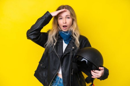 Foto de Rubia inglesa jovencita con un casco de moto aislado sobre fondo amarillo haciendo gesto sorpresa mientras mira a un lado - Imagen libre de derechos