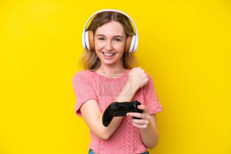 Téléchargez les photos : Blonde Anglaise jeune fille jouant avec un contrôleur de jeu vidéo isolé sur fond jaune célébrant une victoire - en image libre de droit