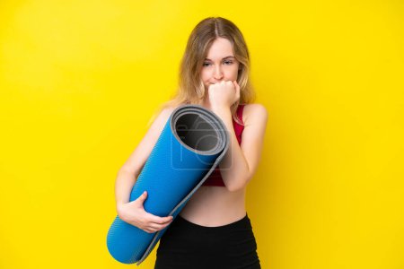 Foto de Young sport caucasian woman going to yoga classes while holding a mat isolated on yellow background having doubts - Imagen libre de derechos