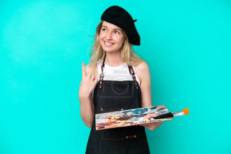 Foto de Young artist caucasian woman holding a palette isolated on blue background pointing up a great idea - Imagen libre de derechos