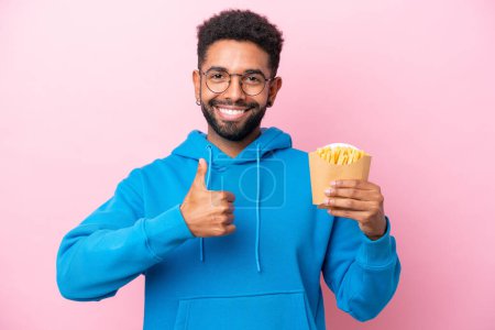 Photo for Young Brazilian man holding fried chips isolated on pink background with thumbs up because something good has happened - Royalty Free Image