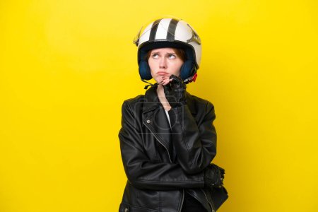 Téléchargez les photos : Jeune femme anglaise avec un casque de moto isolé sur fond jaune ayant des doutes et la pensée - en image libre de droit