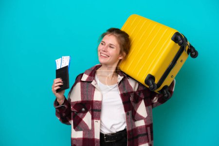 Foto de Joven mujer inglesa aislada sobre fondo azul en vacaciones con maleta y pasaporte - Imagen libre de derechos
