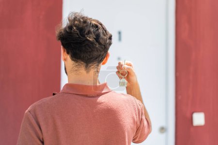 Téléchargez les photos : Jeune homme beau arabe tenant les clés de la maison à l'extérieur en position arrière - en image libre de droit