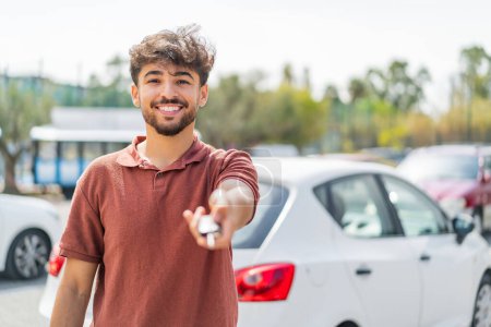Téléchargez les photos : Jeune homme beau arabe à l'extérieur tenant des clés de voiture avec une expression heureuse - en image libre de droit