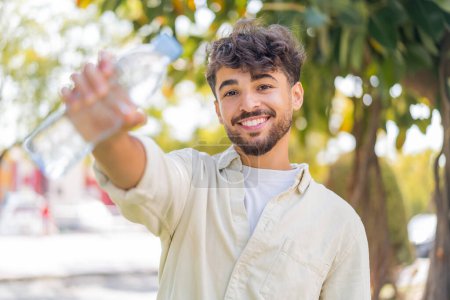Téléchargez les photos : Jeune homme beau arabe avec une bouteille d'eau à l'extérieur - en image libre de droit