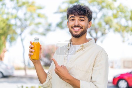 Photo for Young Arabian handsome man holding an orange juice at outdoors and pointing it - Royalty Free Image