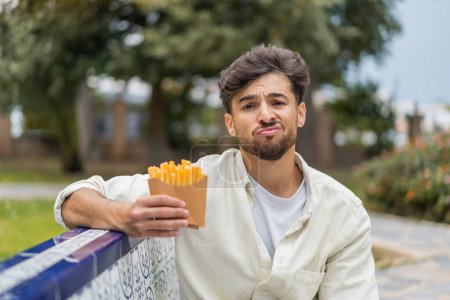 Téléchargez les photos : Jeune homme beau arabe tenant des frites à l'extérieur avec une expression triste - en image libre de droit