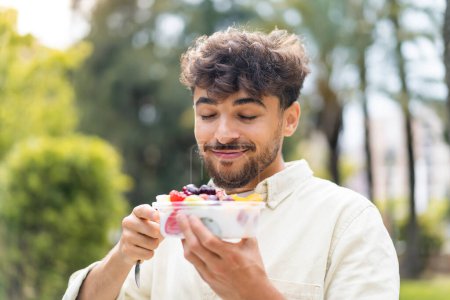 Téléchargez les photos : Jeune homme beau arabe tenant un bol de fruits à l'extérieur - en image libre de droit