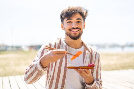 Foto de Hombre árabe guapo al aire libre sosteniendo sashimi - Imagen libre de derechos