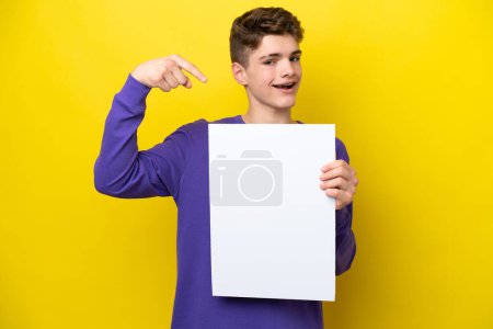 Photo for Teenager Russian man isolated on yellow background holding an empty placard with happy expression and pointing it - Royalty Free Image