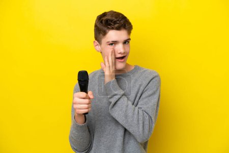 Photo for Singer Teenager man picking up a microphone isolated on yellow background whispering something - Royalty Free Image