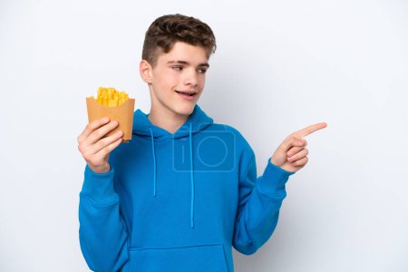 Téléchargez les photos : Adolescent russe tenant des pommes de terre frites isolées sur fond blanc pointant du doigt vers le côté et présentant un produit - en image libre de droit